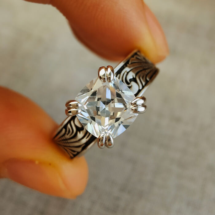 Flower engraved promise ring with clear zircon held between fingers