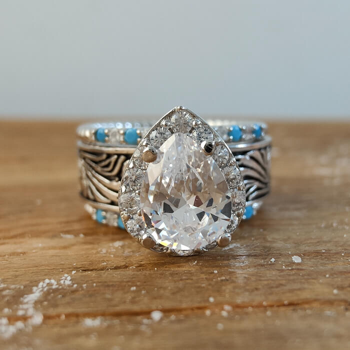 Pear-shaped engagement ring with turquoise accents on a decorative silver band