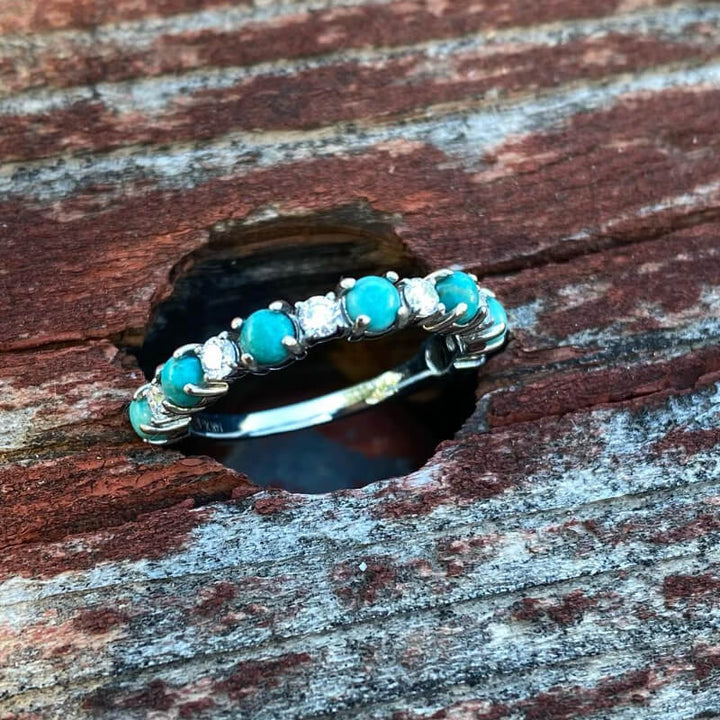 Silver band ring featuring round turquoise and zircon stones on rustic wood.