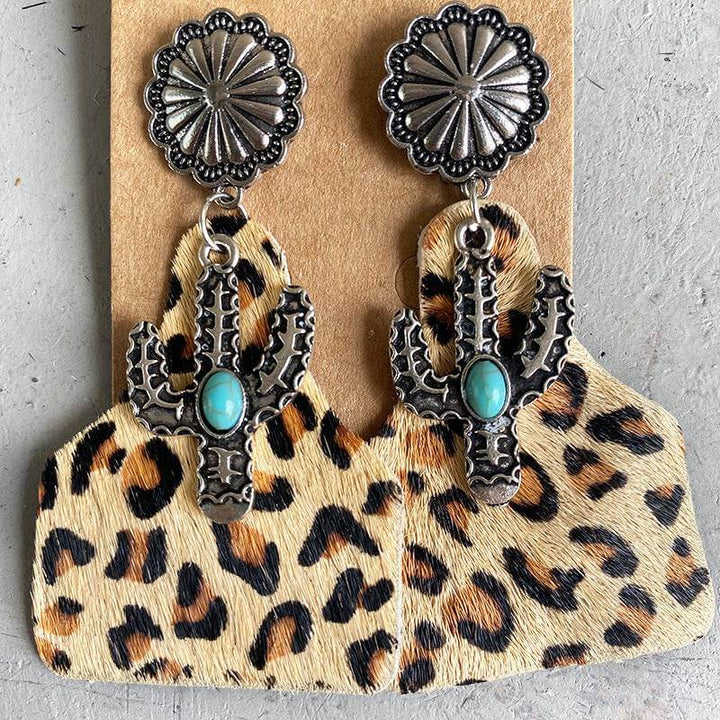 Turquoise cactus earrings with silver embellishments on cowhide print backing.