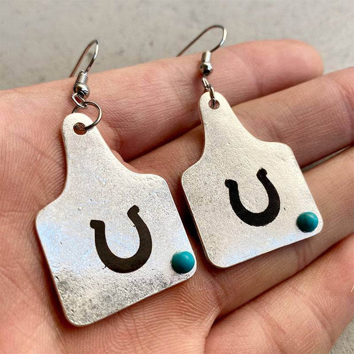 Silver cow tag earrings with a turquoise bead and black U design