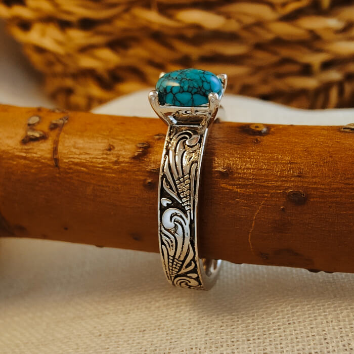 Flower engraved silver ring with turquoise gemstone on wooden surface.