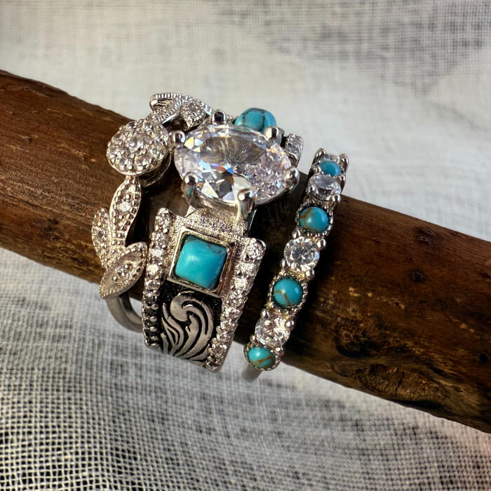 Three vintage rings with turquoise stones and diamond accents on a wooden branch.