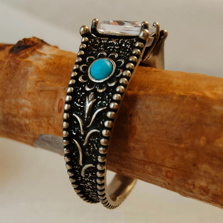 Vintage turquoise engagement ring with intricate floral patterns and clear stone accent.