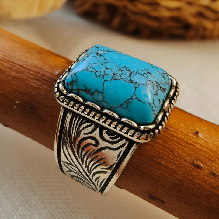 Wide band turquoise ring with intricate silver floral engravings and rectangular stone