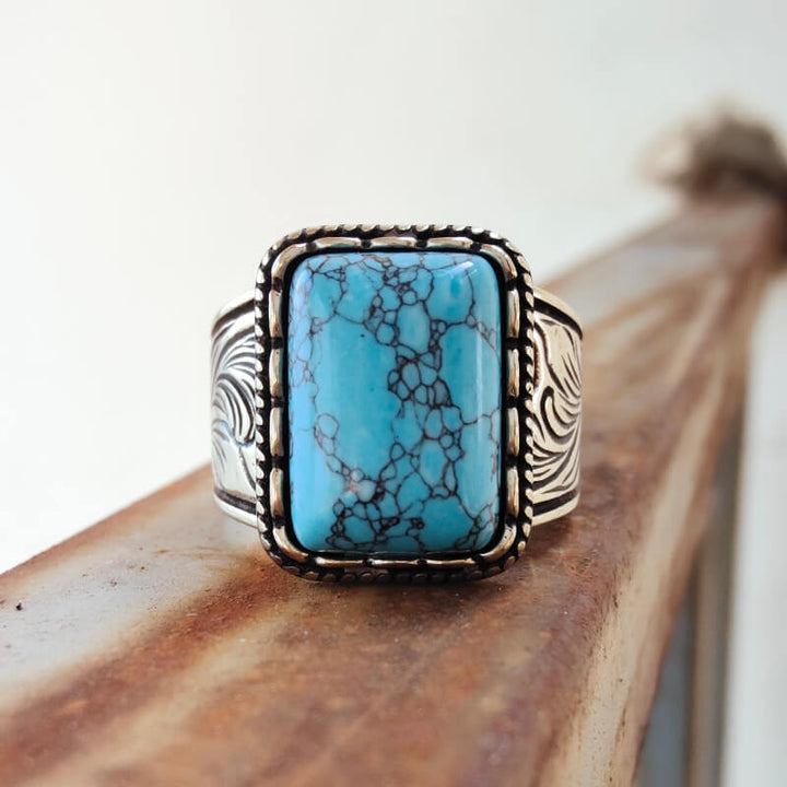 Rectangular turquoise ring with ornate silver band and black veining