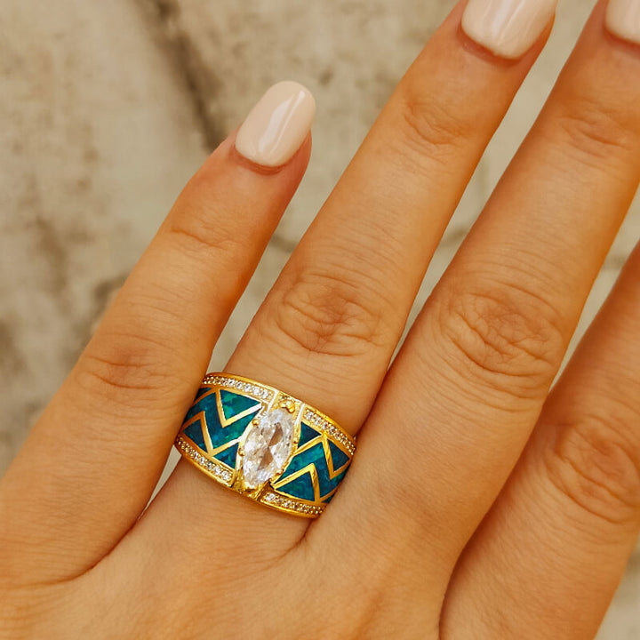 Marquise cut blue opal ring with zircon on a gold zigzag band displayed on a hand.