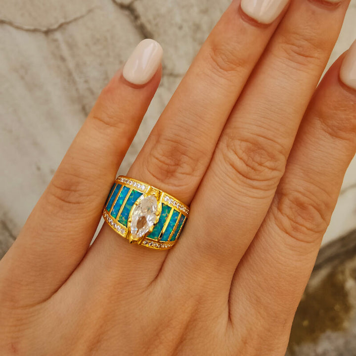 Gold engagement ring with turquoise inlay and marquise zircon stone on a hand.