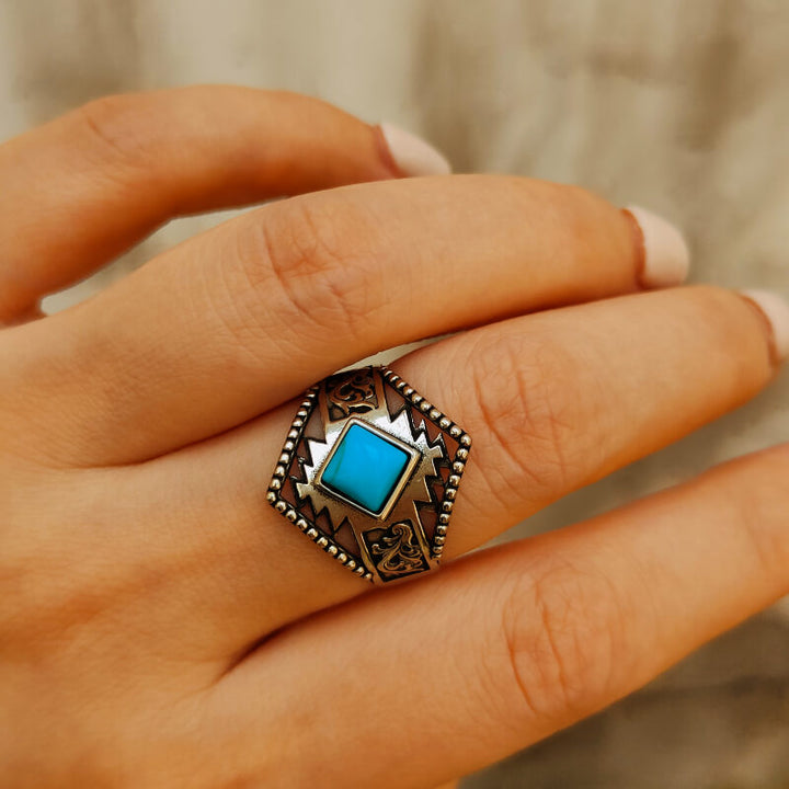Square turquoise ring with silver engravings on a hand