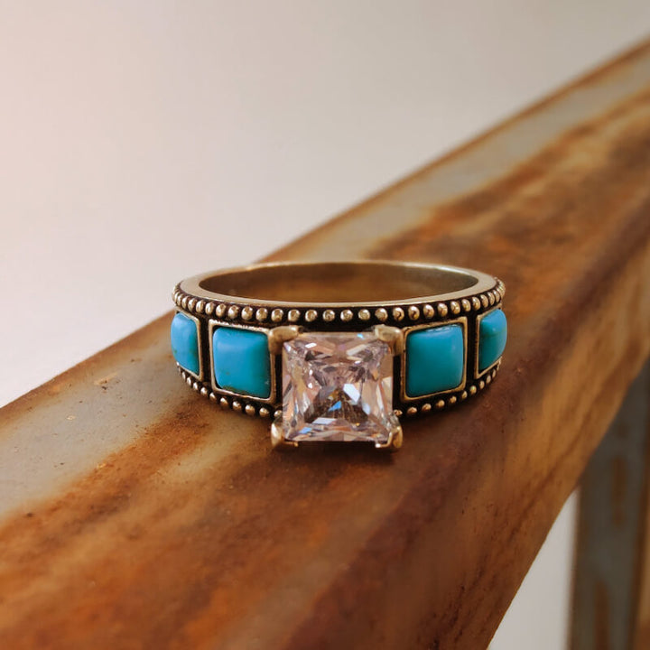 Vintage turquoise zircon ring with square-cut stone on rustic wooden display.