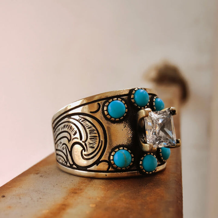 Wide band turquoise ring with diamond centerpiece and detailed floral design.