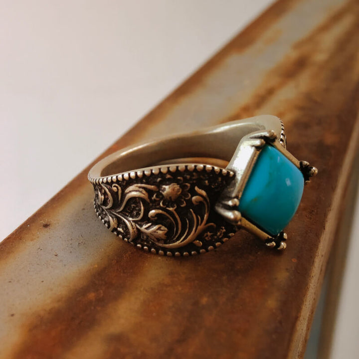 Turquoise square ring with floral engravings in a silver setting.