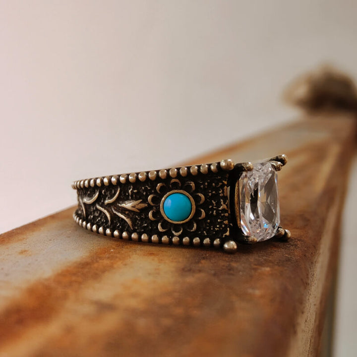 Turquoise and clear stone engagement ring with ornate vintage metalwork.