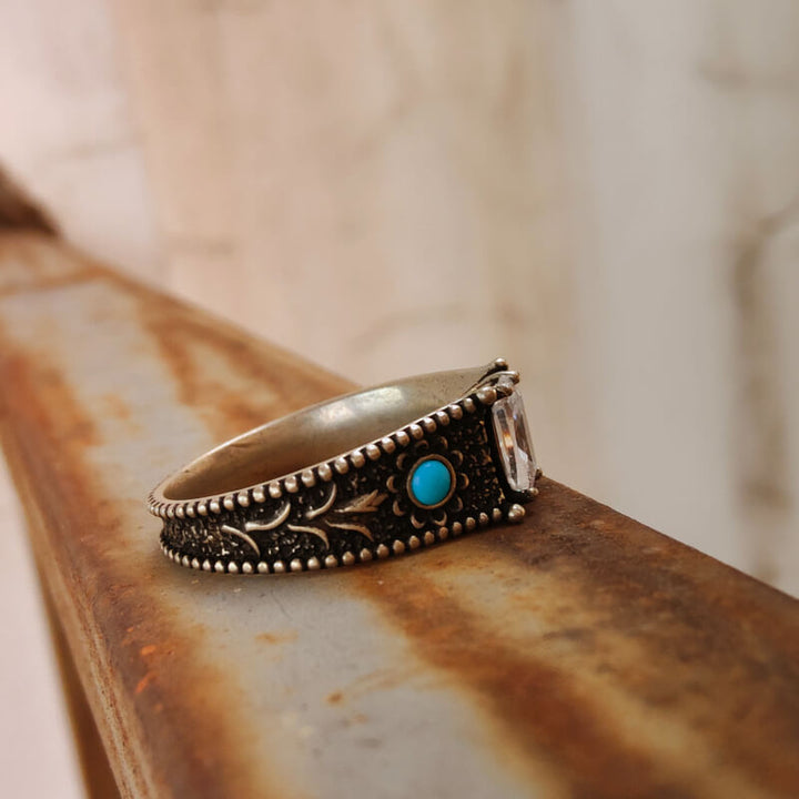 Vintage-style engagement ring with turquoise stone and clear accent on ornate band.