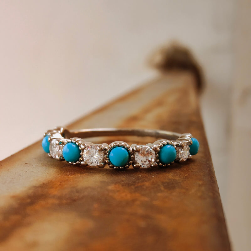 Turquoise and diamond silver band ring on a rustic metal surface