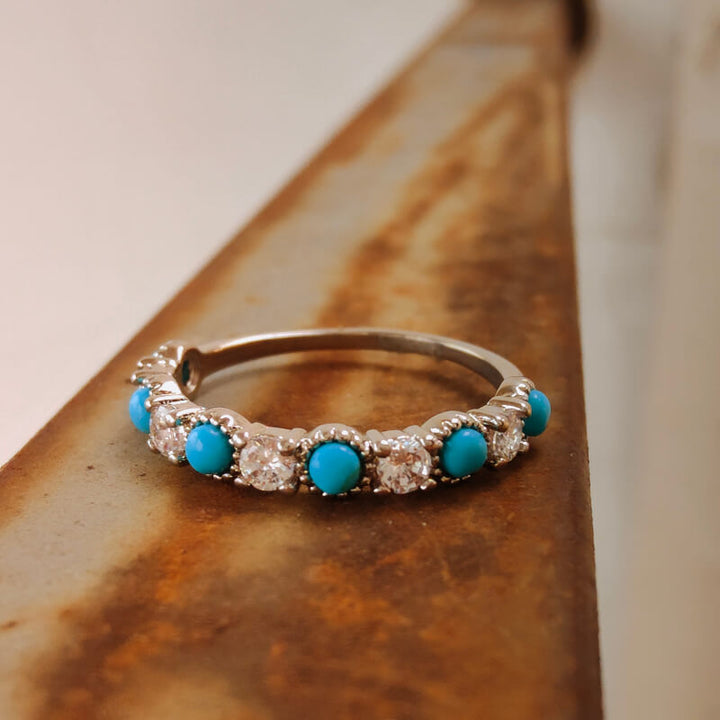 Elegant silver band ring with turquoise and diamond accents on a wooden surface.