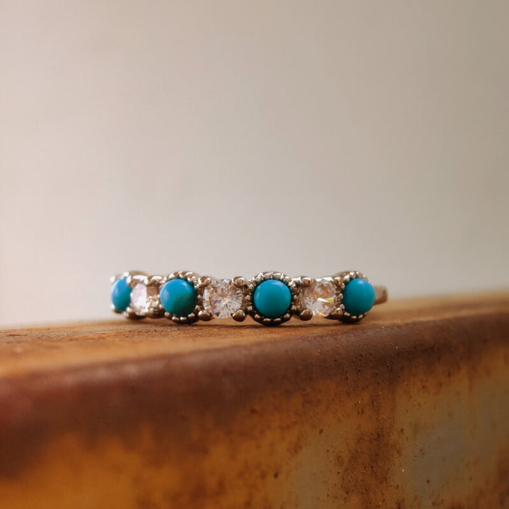 Turquoise and diamond silver band ring displayed on rustic wooden surface.