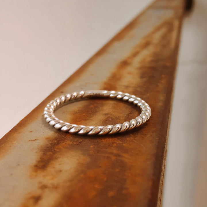 Sterling silver twisted band ring resting on a weathered metal surface