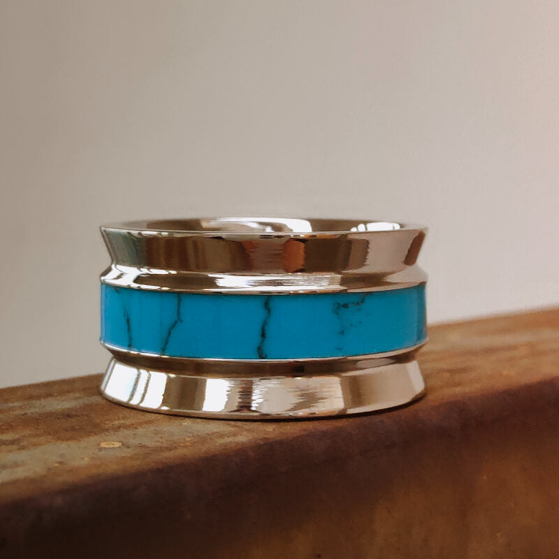 Wide titanium turquoise ring with sleek design on rustic metal background.