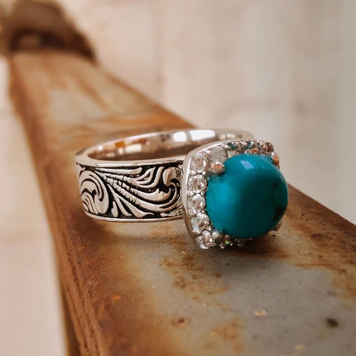 Silver-black ring with flower engravings and a turquoise stone surrounded by a diamond halo.