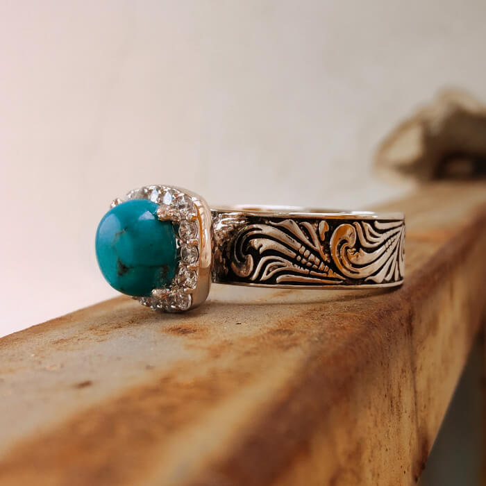 Turquoise ring with floral engravings, diamond halo, and silver-black band.