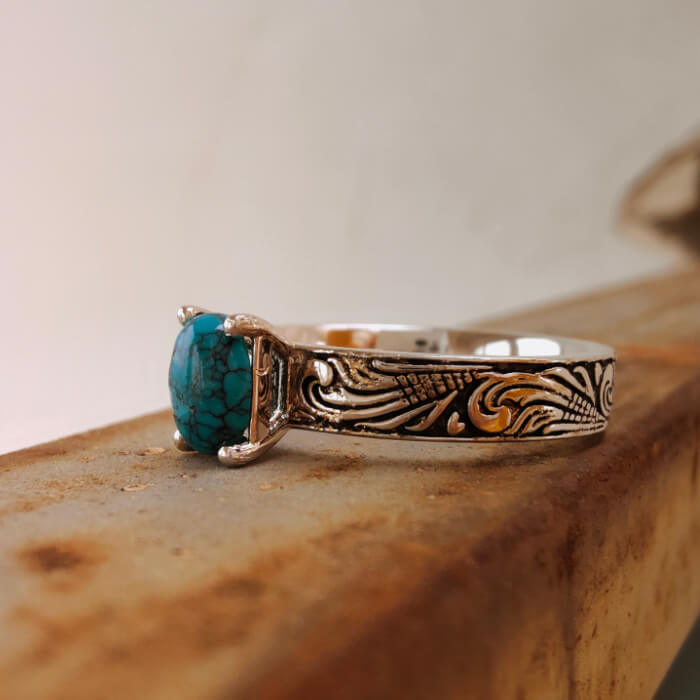 Side view of flower engraved silver ring featuring oval turquoise gemstone.