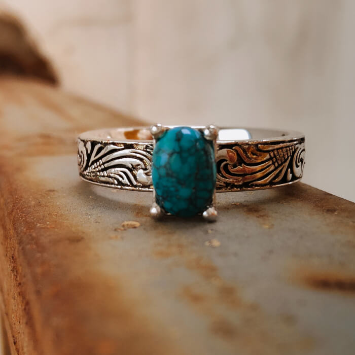 Oval turquoise gemstone set in a silver ring with floral engravings, Western jewelry.