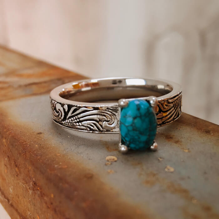 Oval turquoise gemstone on a flower engraved silver ring, showcasing Western style.