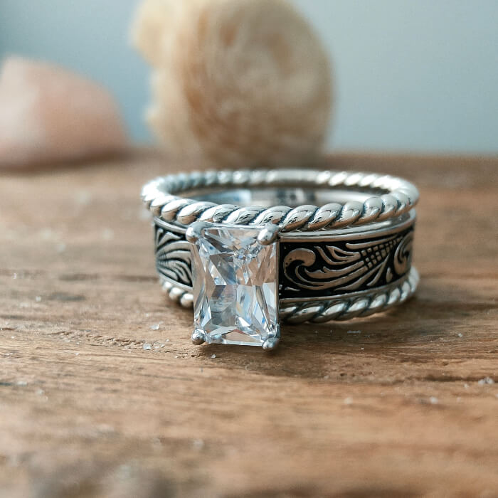 Engraved silver twist band ring with rectangular zircon on wooden surface.