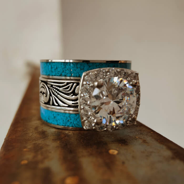 Turquoise ring with diamond halo and silver floral designs on a rustic surface