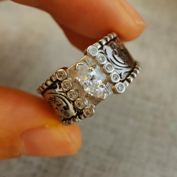 Hand holding wide band silver engagement ring with marquise diamond and detailed engravings