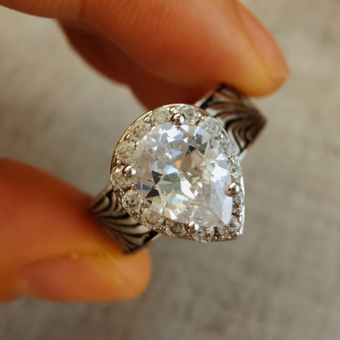 Close-up of a pear-cut diamond ring with intricate silver design and gemstone accents.