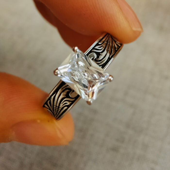 Hand holding Western engagement ring with emerald-cut zircon on engraved silver-black band