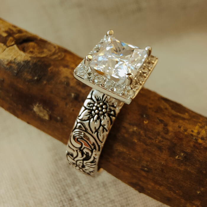 Square engagement ring with floral engraving and diamond halo featuring zircon stone.