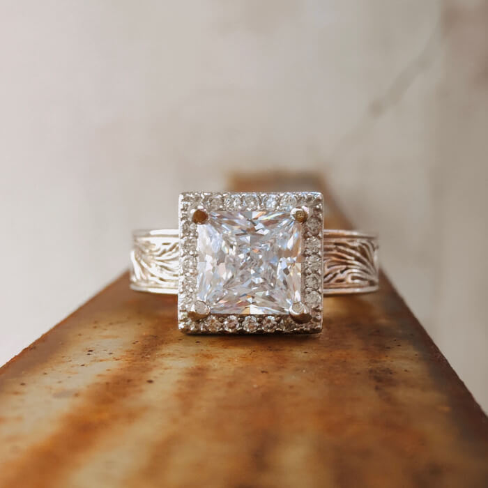 Square diamond ring with zircon center, floral details, placed on metal surface.