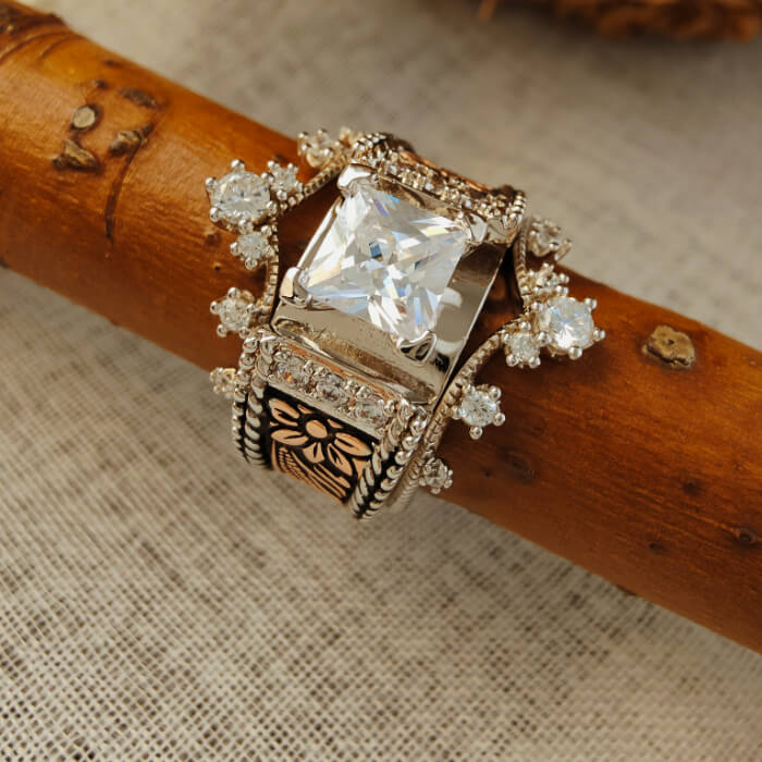 Square engagement ring with floral design and diamond accents on wood