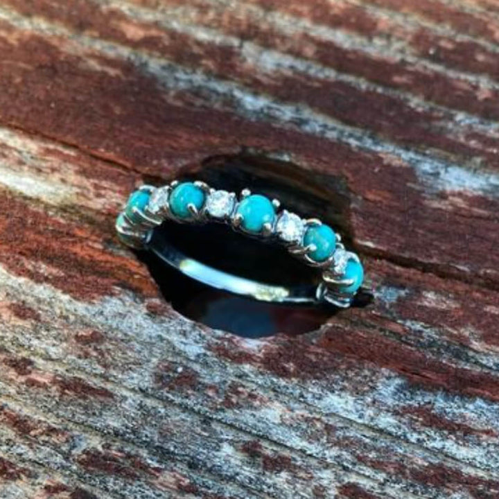 Silver band ring with turquoise and diamond stones on rustic wood.