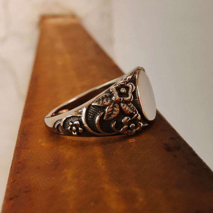 Silver flower engraved band ring featuring a polished surface on a rustic background.