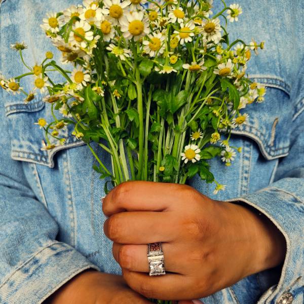Wide band floral ring with zircon worn while holding a bouquet of daisies.