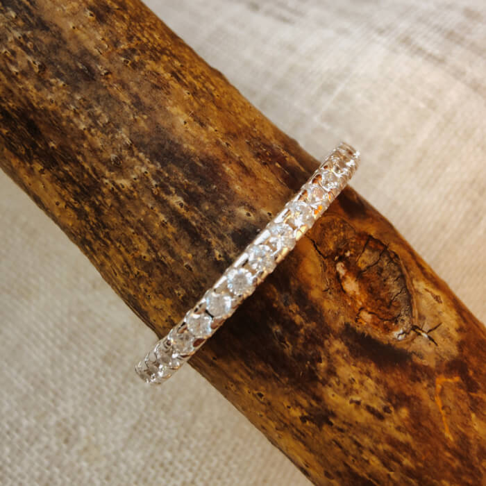 Slim silver moissanite stacking ring band on wooden surface
