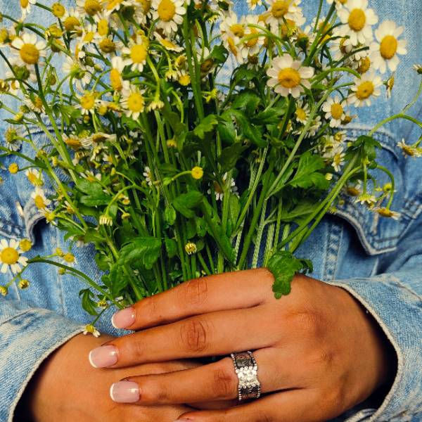 Wide band silver engagement ring with marquise diamond, held among fresh flowers.