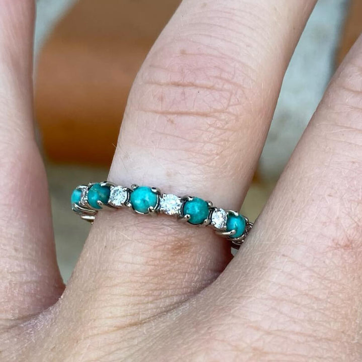 Silver band ring showcasing turquoise and diamond stones on a hand.