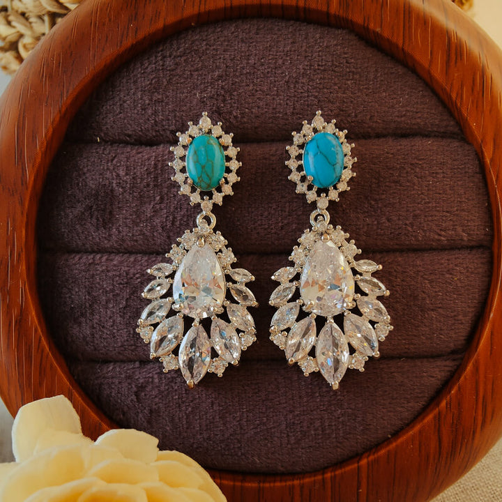 Turquoise and diamond drop earrings on a plush display.