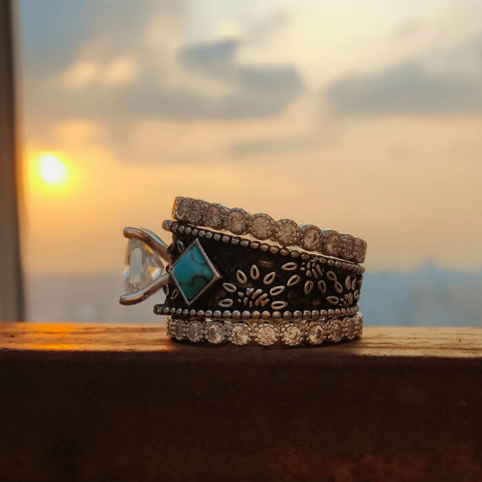 Three stacked vintage turquoise rings with diamond accents against sunset background