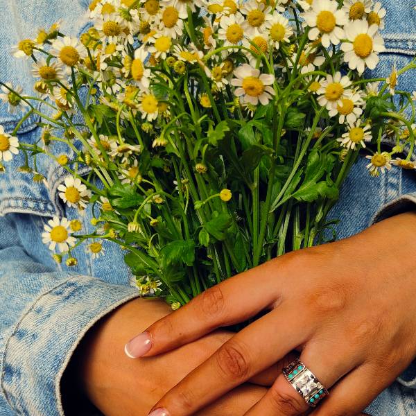 Woman's hand wearing Western turquoise diamond ring with floral design, holding daisies.