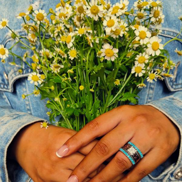 Rose gold turquoise ring on hand holding a bouquet of daisies.