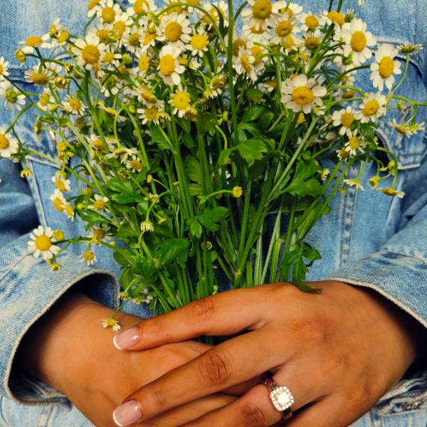 Western engagement ring with diamond halo worn by a person holding a bouquet of daisies