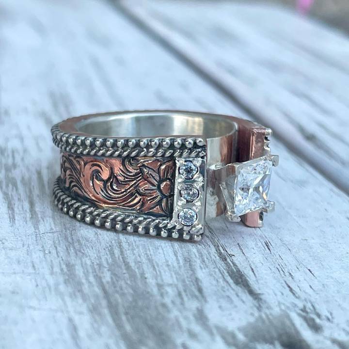 Two-tone floral wide band ring with square zircon and diamond accents on wood.
