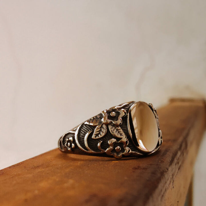 Flower engraved silver ring with a polished stone on a wooden background