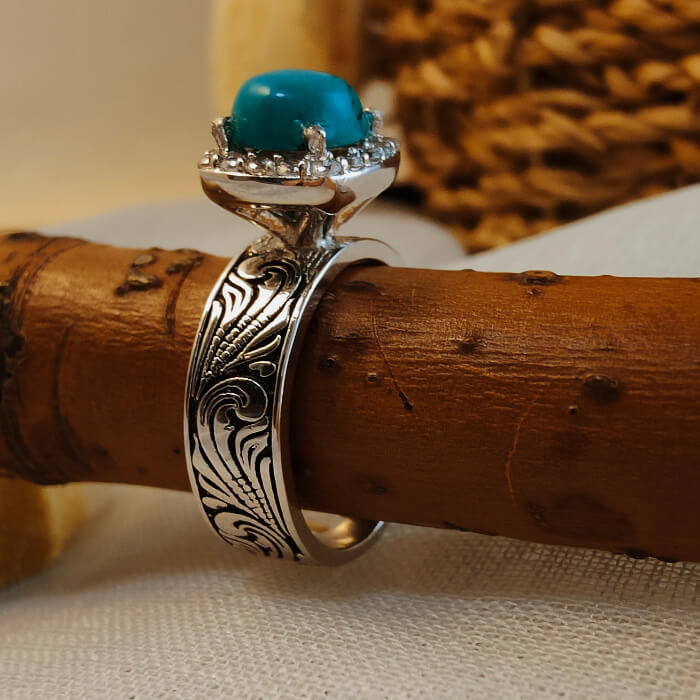 Turquoise ring with floral engravings and diamond accents on a silver-black band.